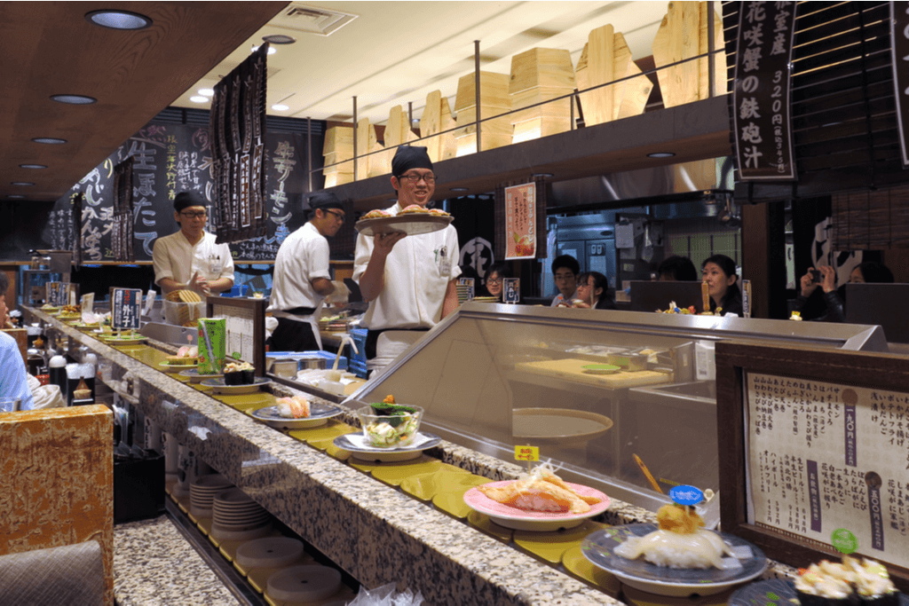 Sushi chefs work behind the counter of of one of Japan's conveyor belt sushi restaurants as customers sit, eat, and chat.