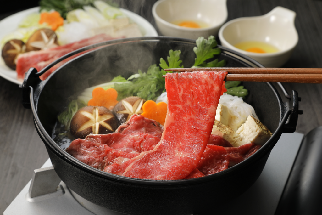 A bowl of sukiyaki hotpot, which feature thing beef strips;.