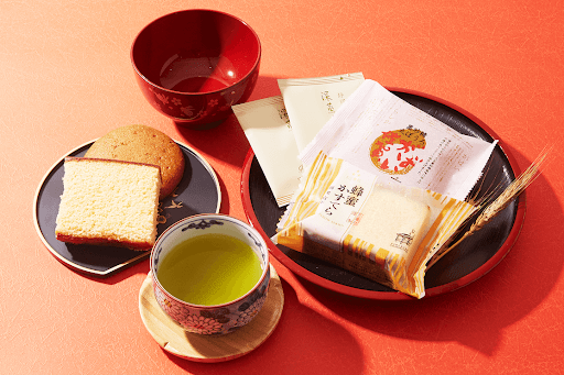 A plate of castella cake with green tea and matching plates. 