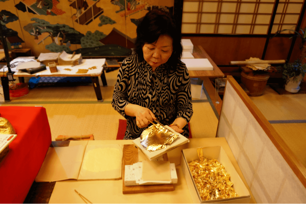 An elder woman manipulating gold leaf. She's a local Japanese maker.