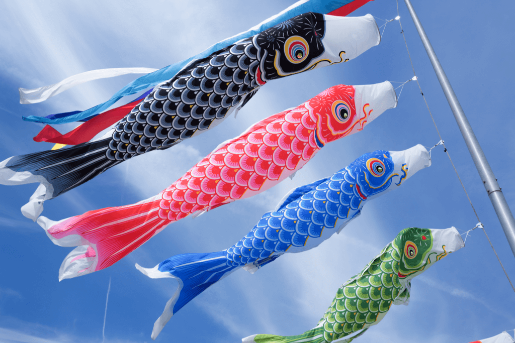 Four koi fish-shaped streamers made for Children's Day hang from a pole and flap in the wind with the colors of the koi fish being black, red, blue, and green from top to bottom.