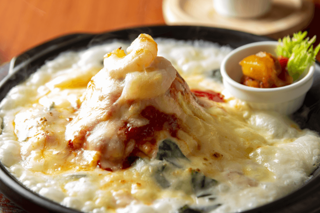 Seafood doria, one of the Western-inspired Yokohama foods, sits on a black plate with cheese, vegetables, and shrimp piled on top of rice.