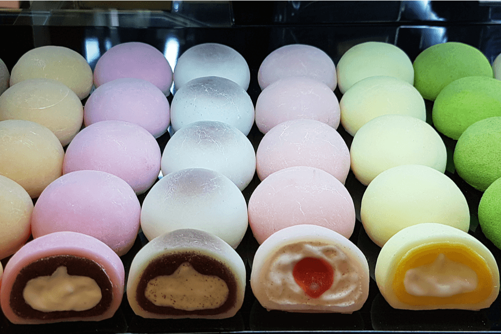 Many rows of daifuku mochi, mochi foods usually stuffed with sweet bean paste, on display in a store with many colors and different fillings.