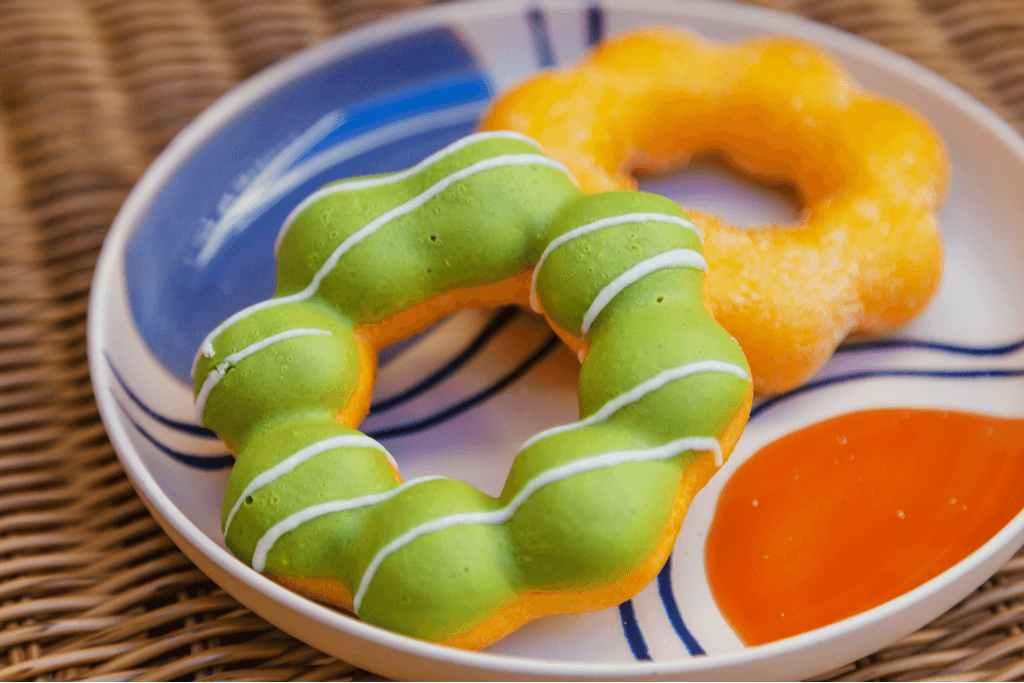 Two different mochi donuts, one of the most popular mochi desserts, sit on a plate, one with a sugar coating and the other with a green tea-flavored frosting
