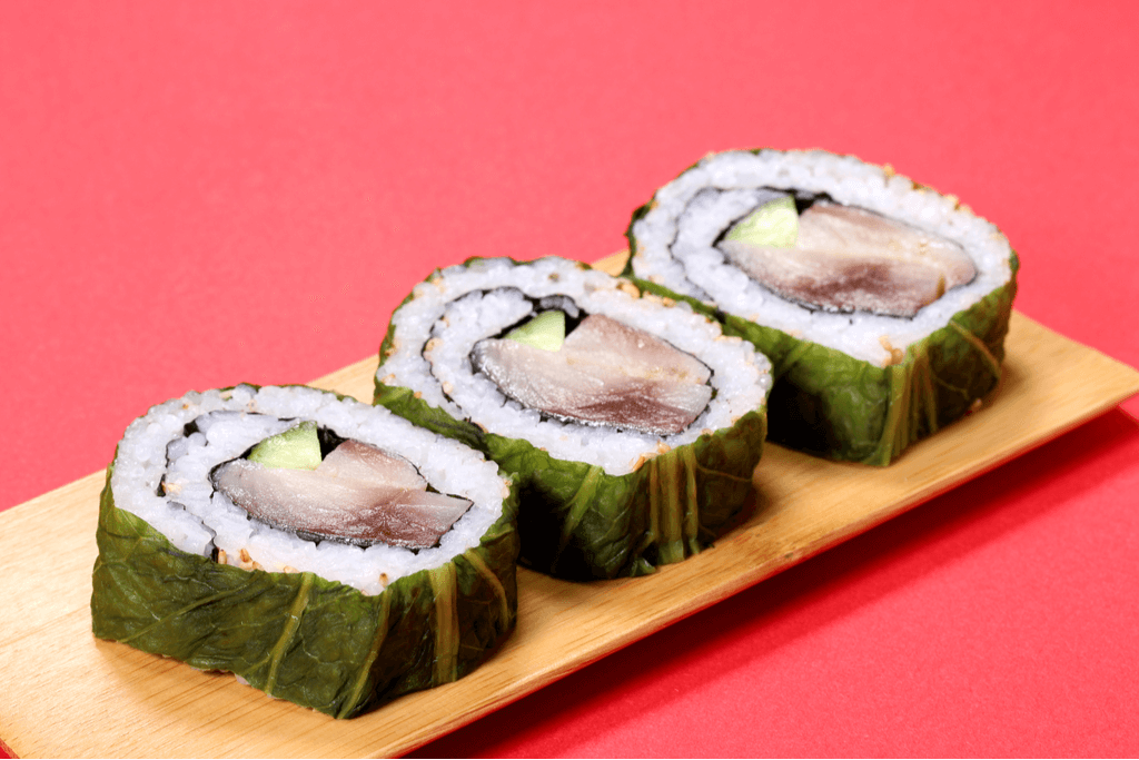 Three pieces of Kyoto-style sushi, with mackerel, cucumber, and rice rolled up inside of kelp, on a wooden sushi-serving plate