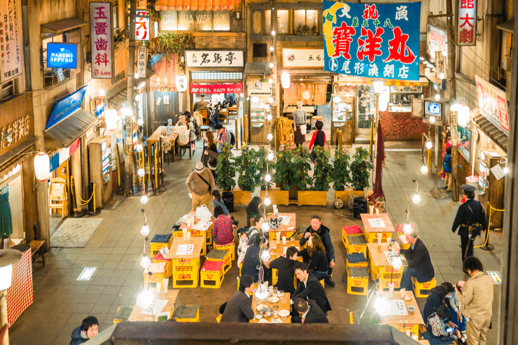 Many people sit in the eating area of the Shin-Yokohama Ramen Museum, one of the Yokohama Museums about ramen, with many noodle shops surrounding the seating area.