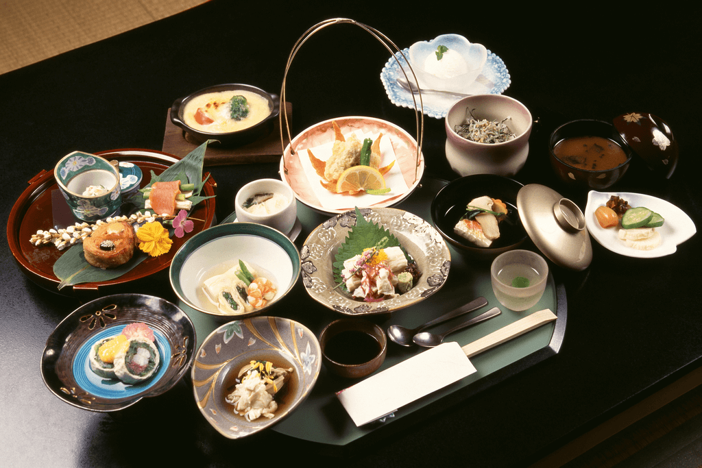 A table with a full course of kaiseki ryori, Kyoto foods made with seafood and vegetables, on many different plates and serving trays.