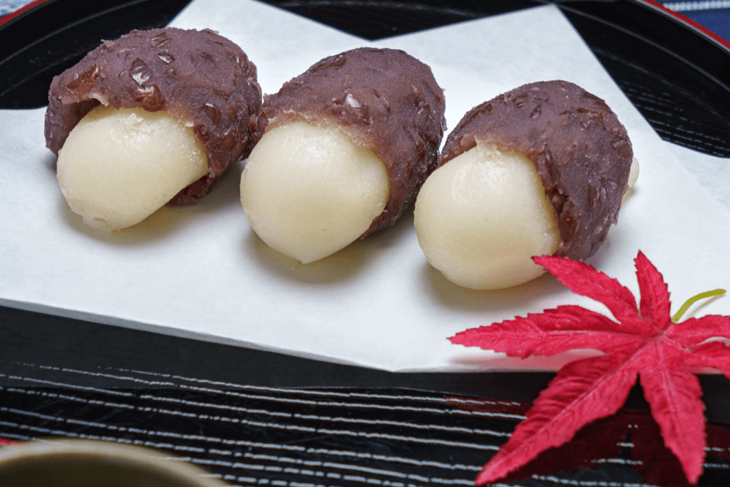 A black tray with white paper and a red leaf with Ohagi, a mochi dish wrapped in red bean paste which is eaten for fall or Tsukimi festivals.