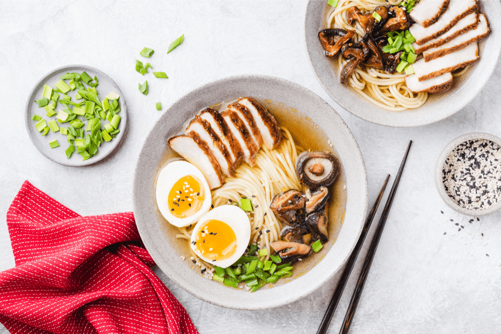 A bowl of chashu (pork belly) ramen with shiitake mushrooms, a split boied egg, and chives, topped with black sesame seeds, a major part of japanese cuisine.