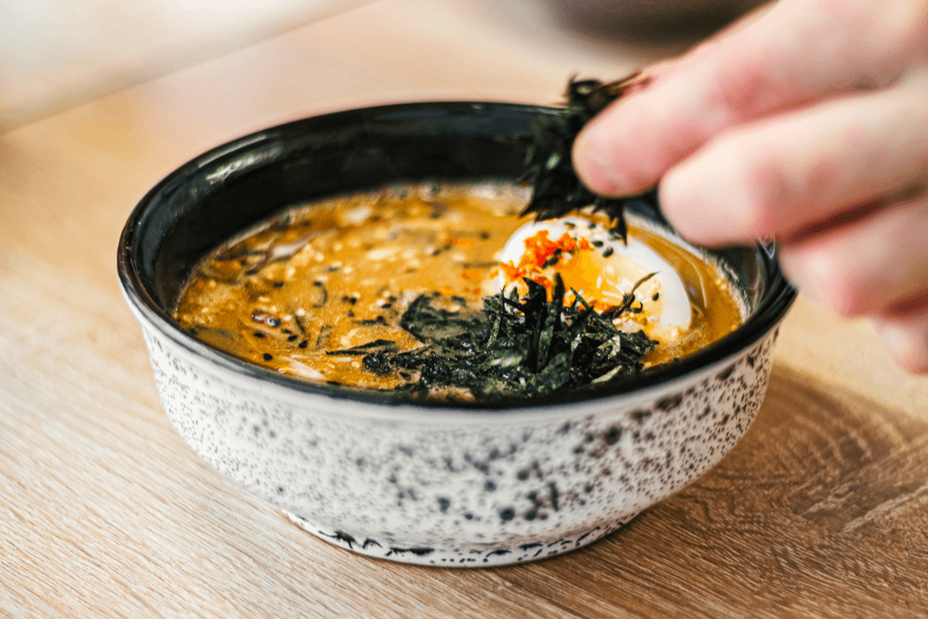 Seaweed is dropped into a small, savory bowl of miso soup with a boiled egg and topped with black sesame seeds, a staple of Japanese cuisine.
