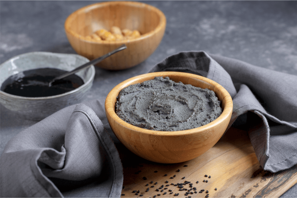 An image of black sesame paste, soy sauce, and soybeans in separate wooden bowls.