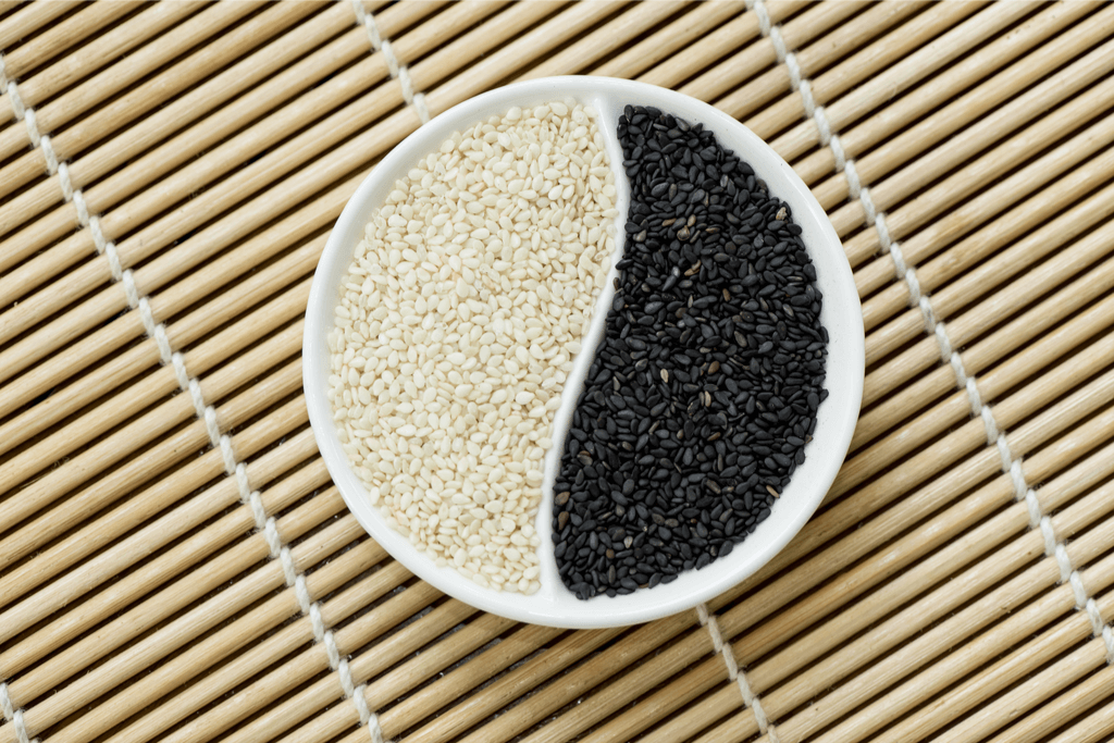 White and Black sesame seeds in a round ying and yang bowl atop of a bamboo mat