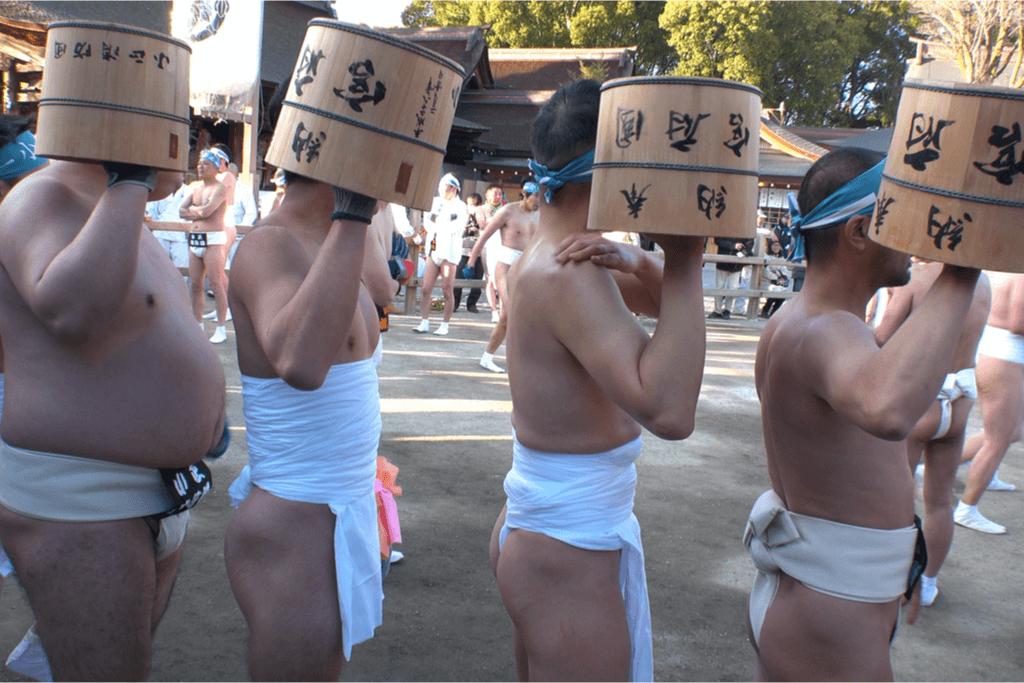 A bunch of men at the "Naked" festival wearing white fundoshi loincloth--a type of tradtional Japanses clothing-- as they hoist wooden buckets.