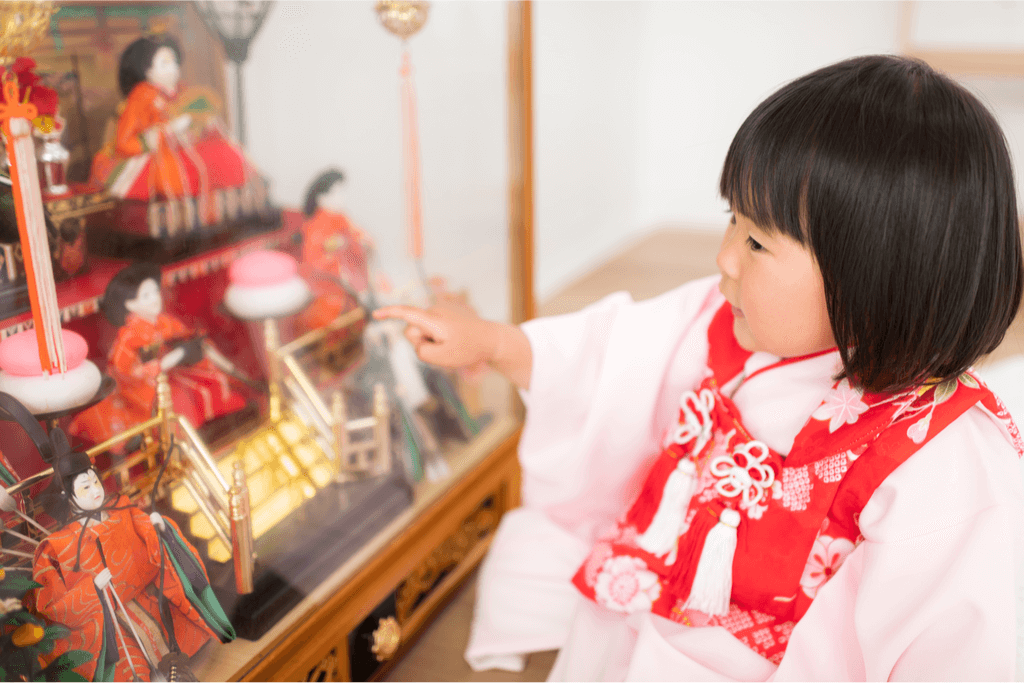 A young girl dressed in a pink kimono places her hina matsuri dolls on a platform.