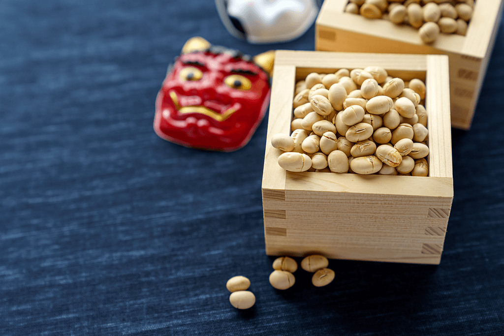 A small box of dried, irimame soybeans next to a small oni mask.