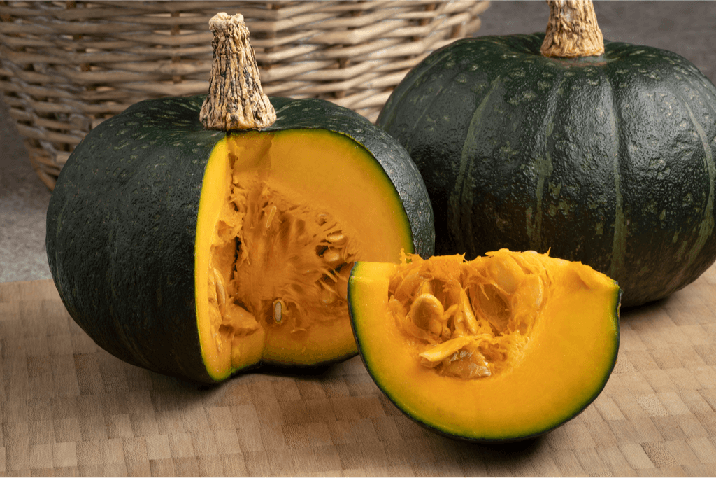 A close-up photo of kabocha pumpkin, which has green skin and orange flesh.