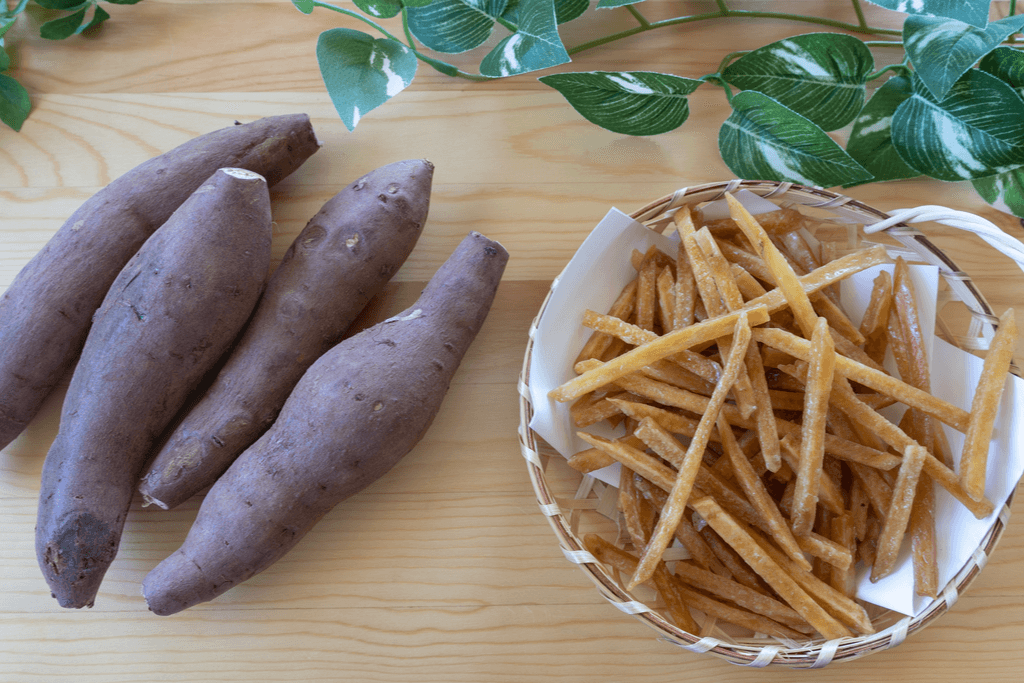 A handful of sweet potatoes next to a bowl of crispy kenpi sweet potato fries.