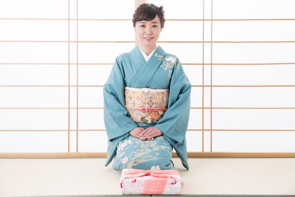 A woman wearing a soft, light blue houmongi kimono with an ornate gold sash.