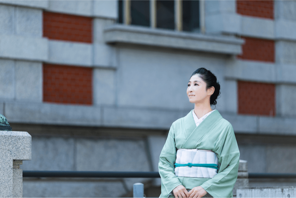 A woman near Tokyo Station wearing a light green, casual tsumugi kimono, which is a form of traditional Japanese clothing.