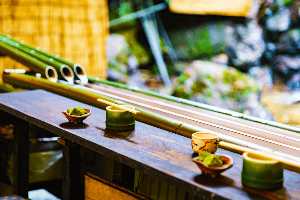 A photograph of a wooden table in front of a bamboo slide for nagashi somen , a fun and popular way to eat food in Kyoto.