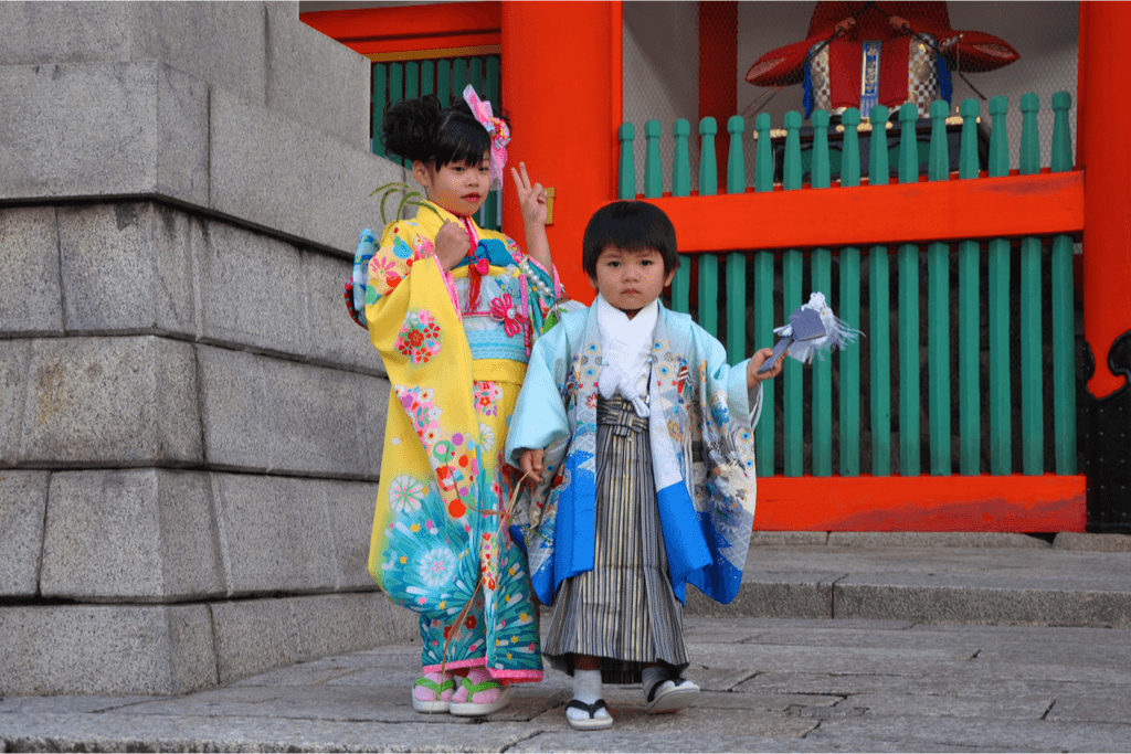 A girl and a boy dressed in a kimono and hakama respectlively outside of a Shinto shrine.
