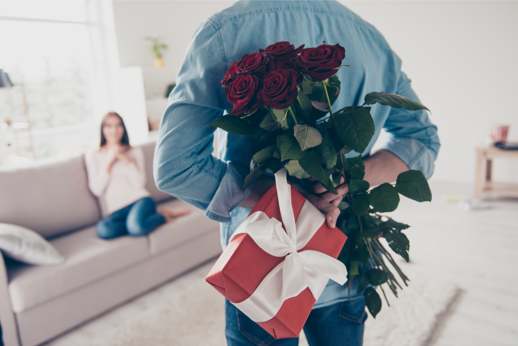 A photogaph of a man hiding some roses and gifts behind his back for White Day.