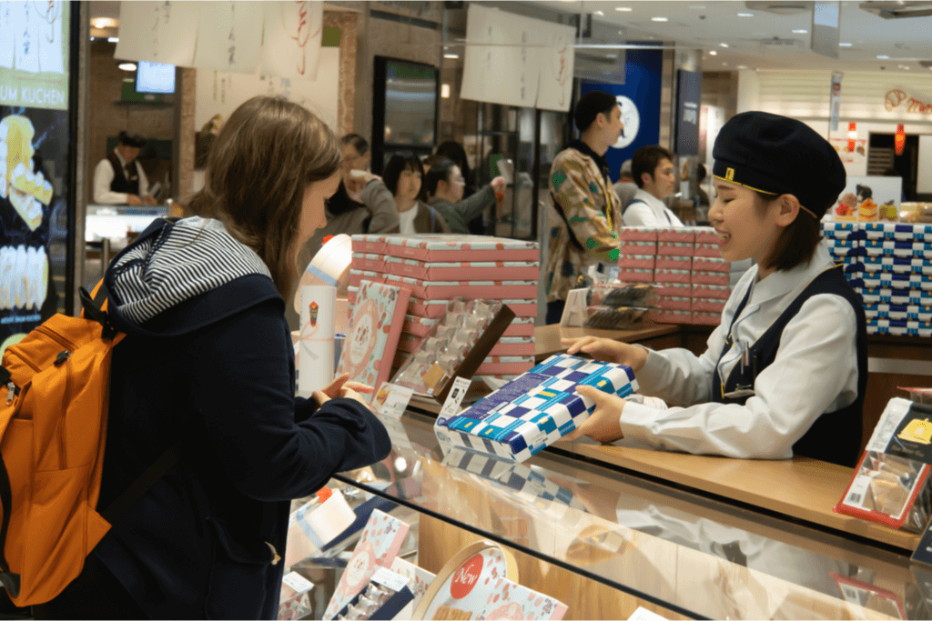 An omiyage (Japanese souvenir) goods shop clerk presenting a consumable product to a customer to give as a present for a Japanese Housewarming Gift Giving