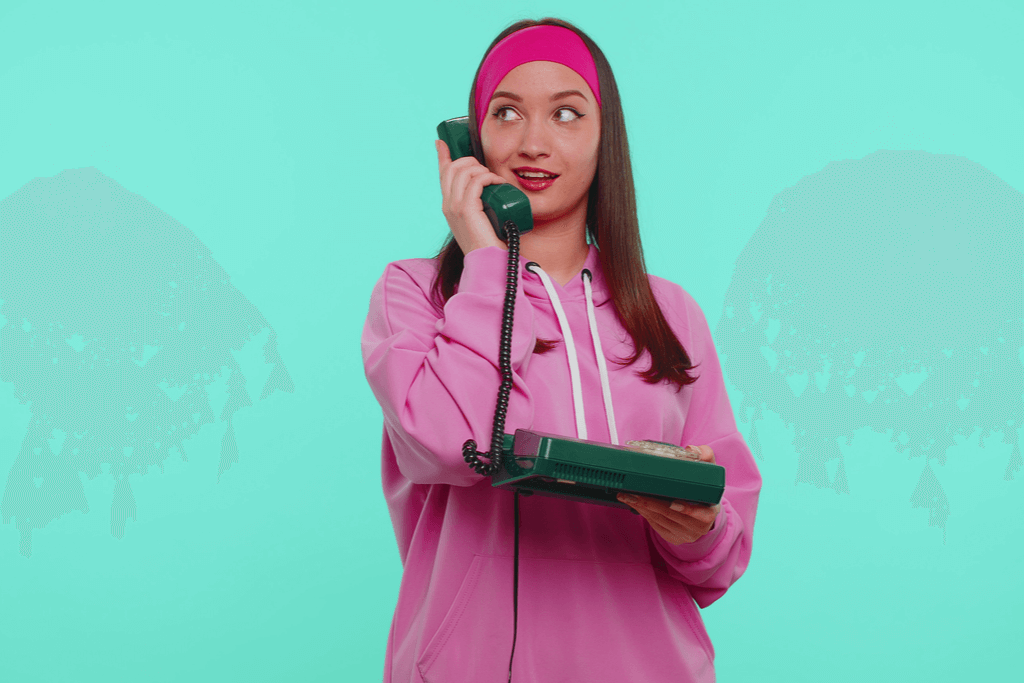 A woman wearing a pink hoodie holding a red corded phone.