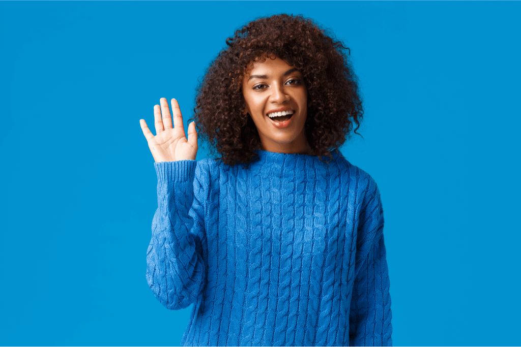 A woman wearing a blue sweater with a blue background giving a friendly wave.