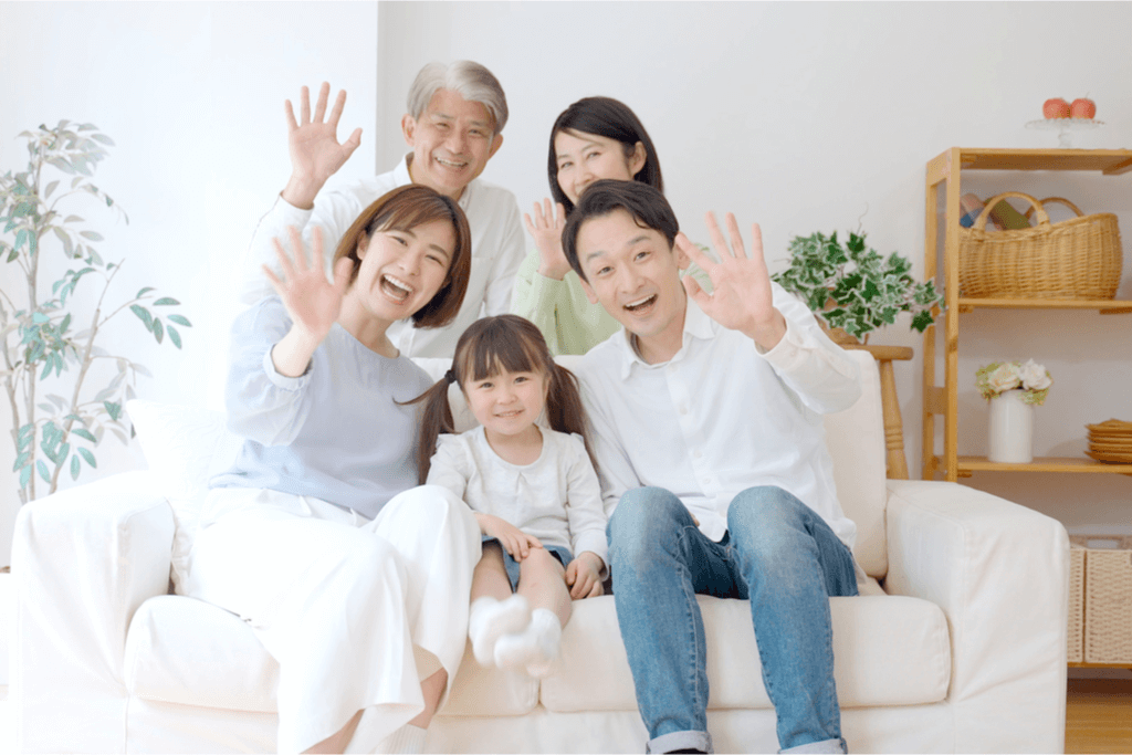 An Asian family on a couch waving with smiles. This is one of many popular Japanese greetings.