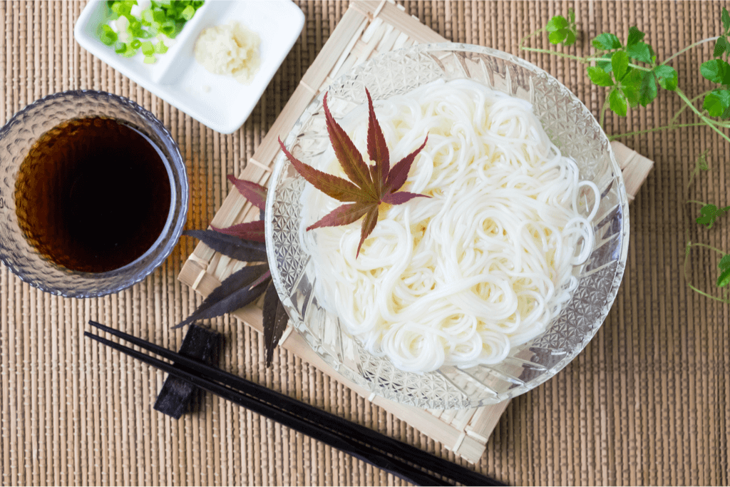 A clear bowl of somen noodles with black chopsticks on the side