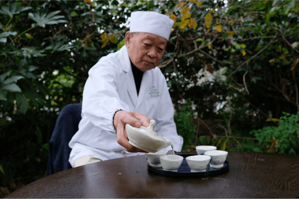 A tea master derssed in white, delicately pouring cups of gyokuro tea into cups. Some gyokuro is hand rubbed tea.