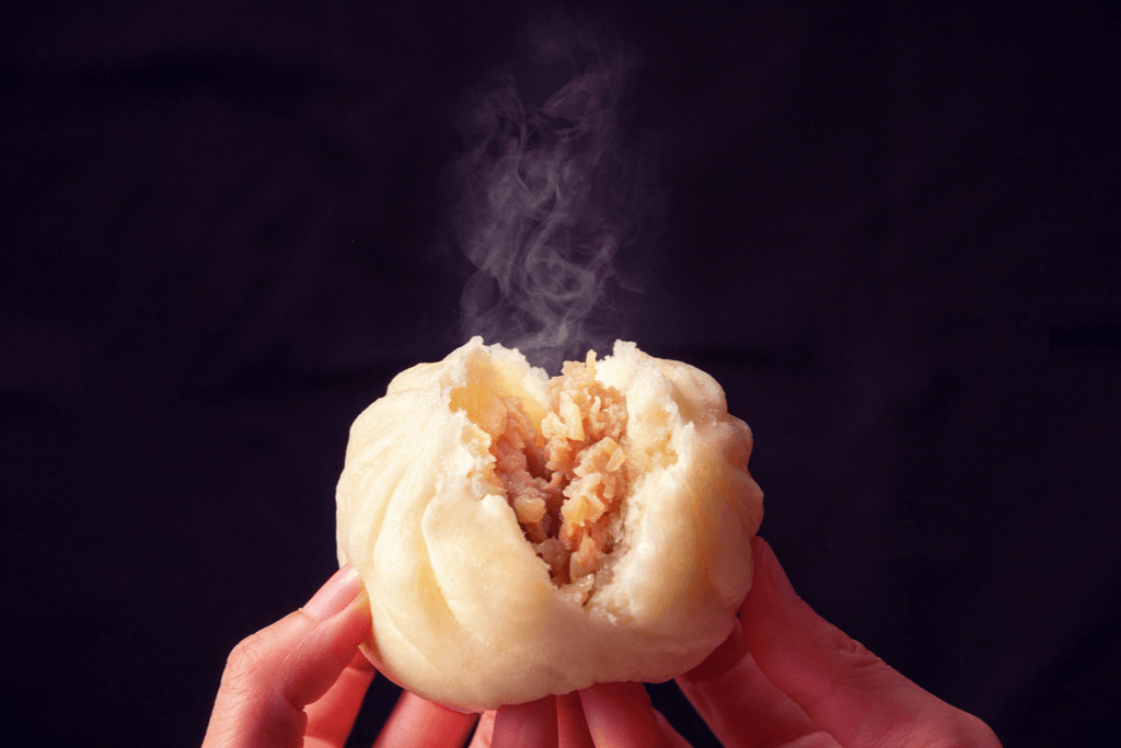 Hands opening up a nikuman, a large steamed bun with meat inside. This is one of many warm traditional Japanese foods.