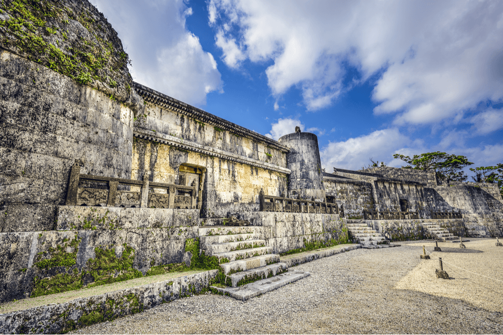 A wide shot of Gyokuun Mauseoleum, a relic from the Ryukyu Kingdom era. It is a large, gray structure against a lighly overcast blue sky.