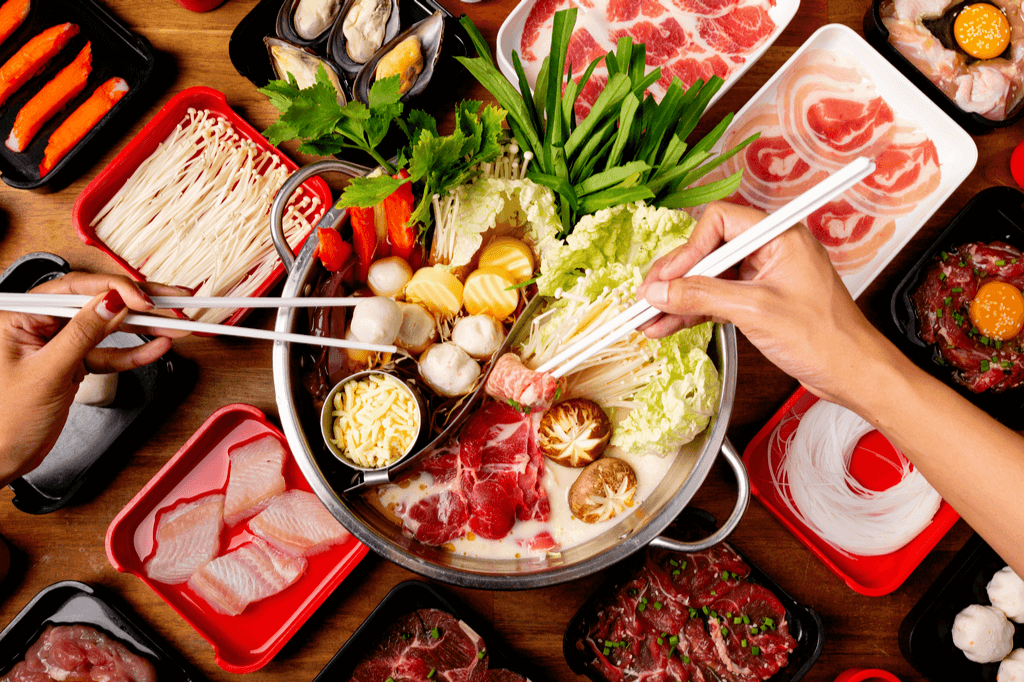 A bunch of people eating shabu shabu , which is an assortment of vegetables and meat that you dipping in boiling hot broth.