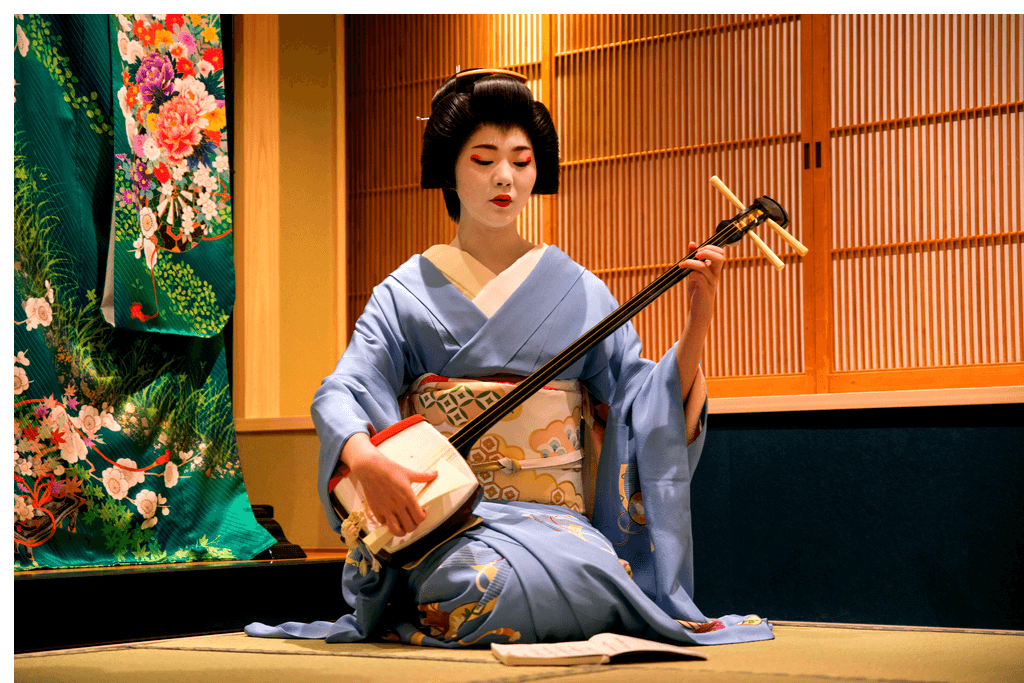 A geisha in a blue kimono playing the shamisen in a tatami room.