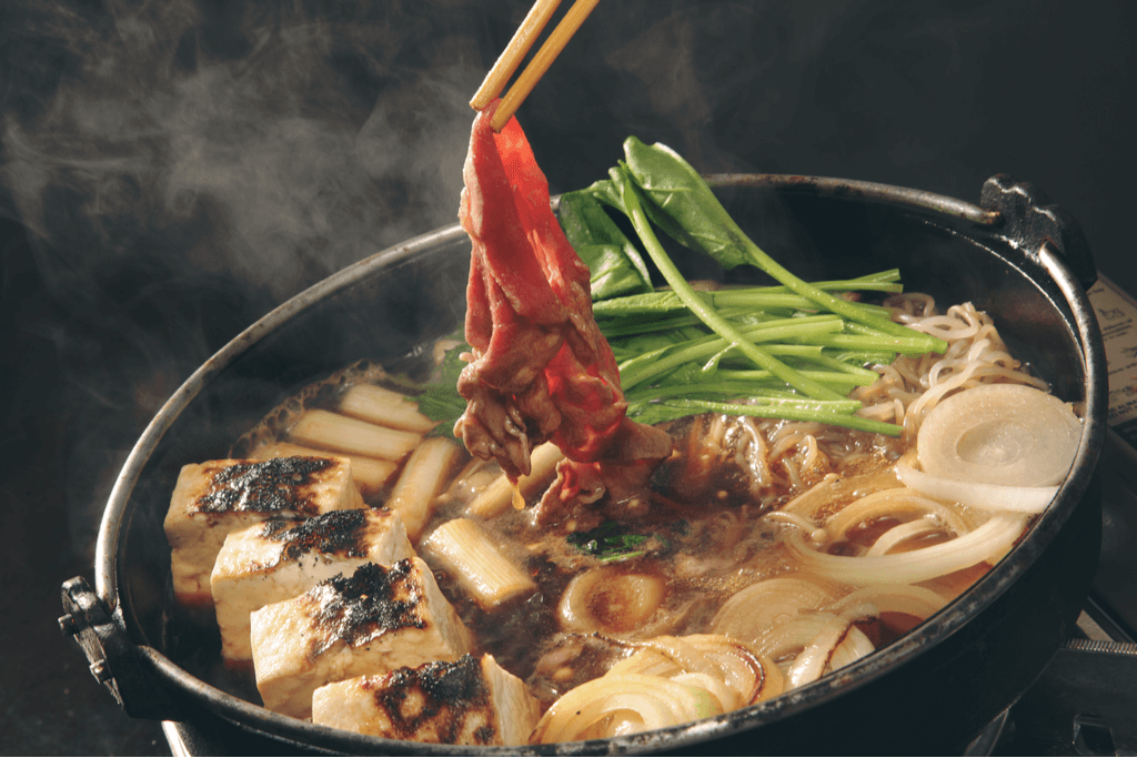 A steaming bowl of sukiyaki, a traditional Japanese food. There's seared tofu, vegetables and meat.
