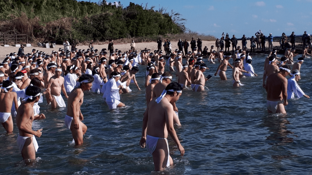 A bunch of men in fundoshi and women in robes in the sea at one winter festivals called the Aoshima Naked Man Festival.
