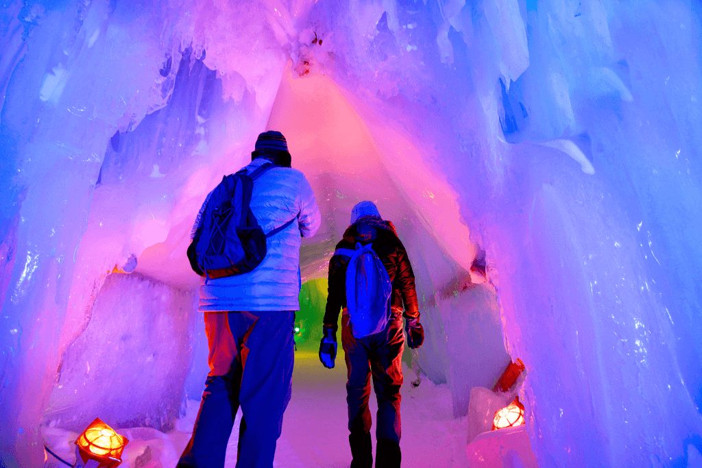 An adult and child entering a purple-illuminated snow cavern. This is at the Sapporo Snow Festival.
