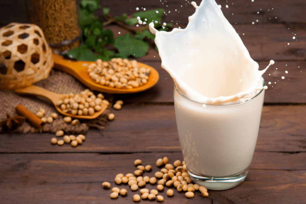 A glass o soymilk splashing everywhere, with some soybeans on the side.