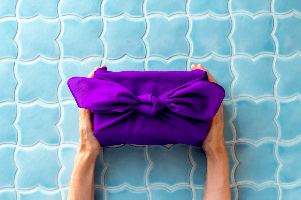 A pair of hands holding a royal purple cloth against a sky blue tile background.