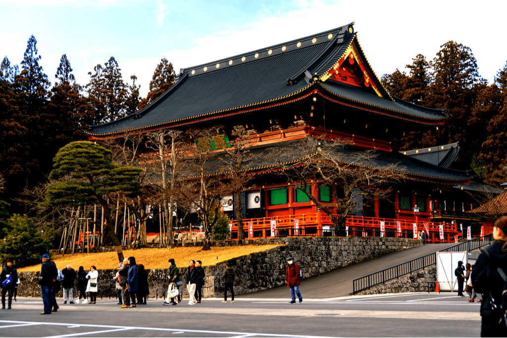 Exterior shot of Rinnoji Temple in Nikko, Japan. A bunch of people are gathered on its front steps.