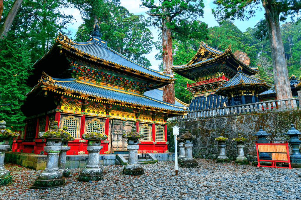 Exterior shot of Toshogu Shrine, a traditional shrine of red and gold in the middle of a forest.