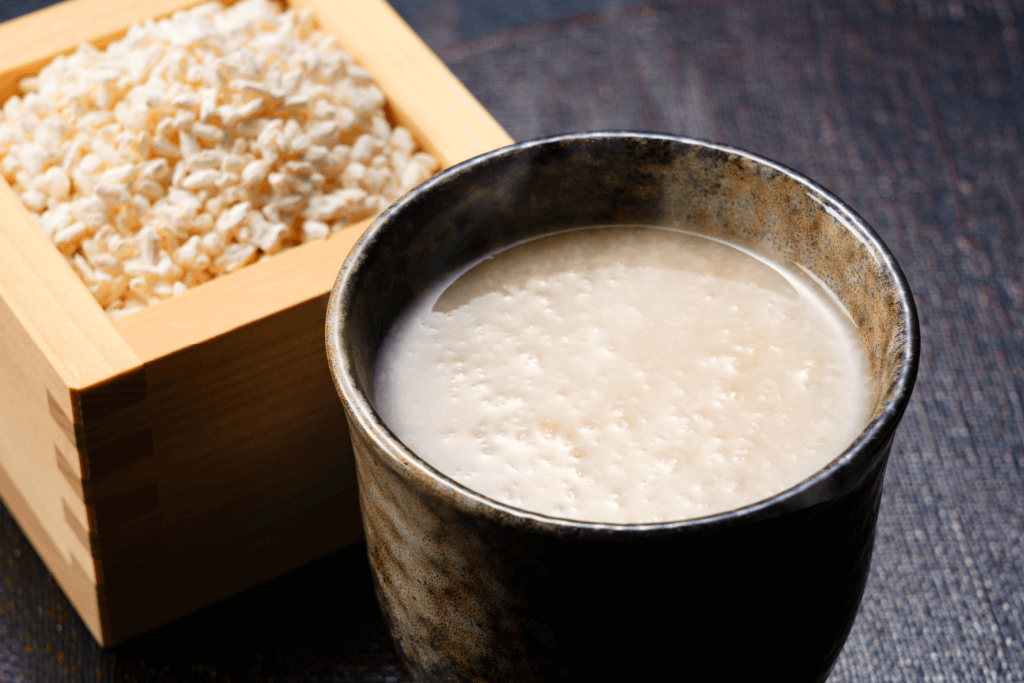 A warm cup of white amazake with a box of koji in the background.