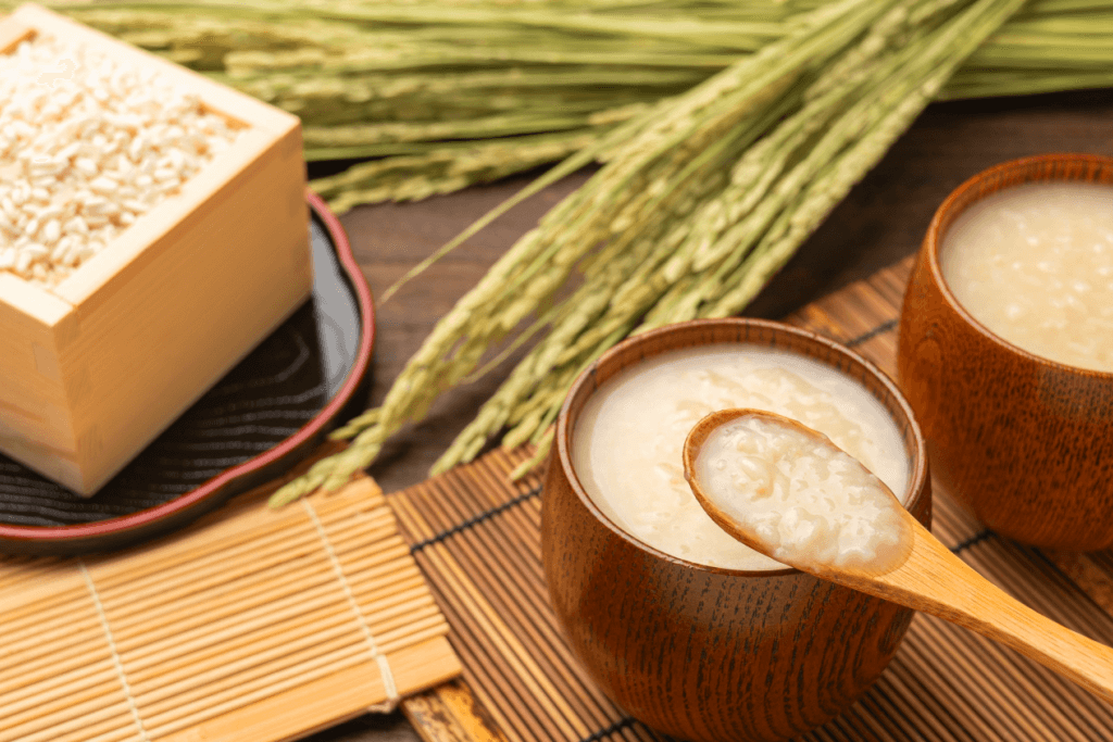 Cups of creamy white amazake, a box of koji, and harvested rice in the back.
