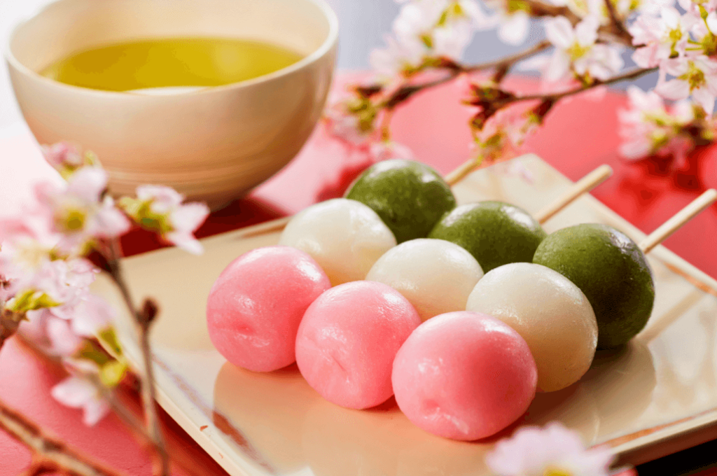 A plate of hanami dango (pink green white) next to some cherry blossoms.