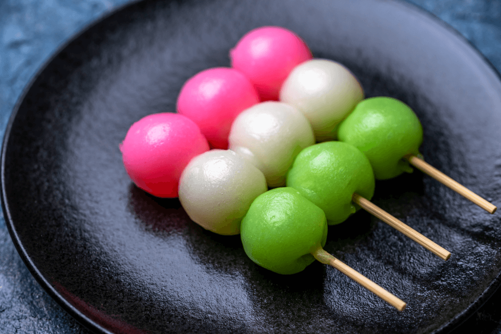 A plate of hanami dango (pink white green mochi) on a black plate. They are on skewers and eaten during spring in Japan.