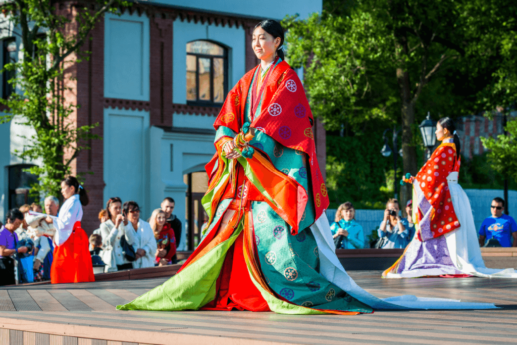 A woman wearing a colorful junihitoe (12-layer kimono) in a town square.