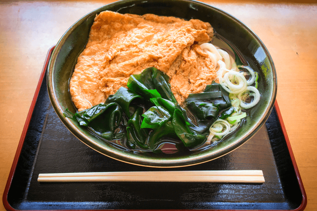 A bowl of kitsune udon which has thick noodles, seaweed and fried tofu. Takoyaki is just as famous as this dish.