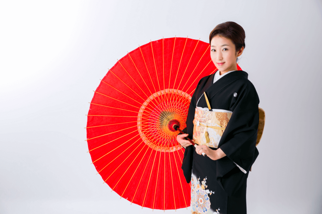 A woman wearing a kurotomesode *black formal womens kimono) while holding a red parasol.